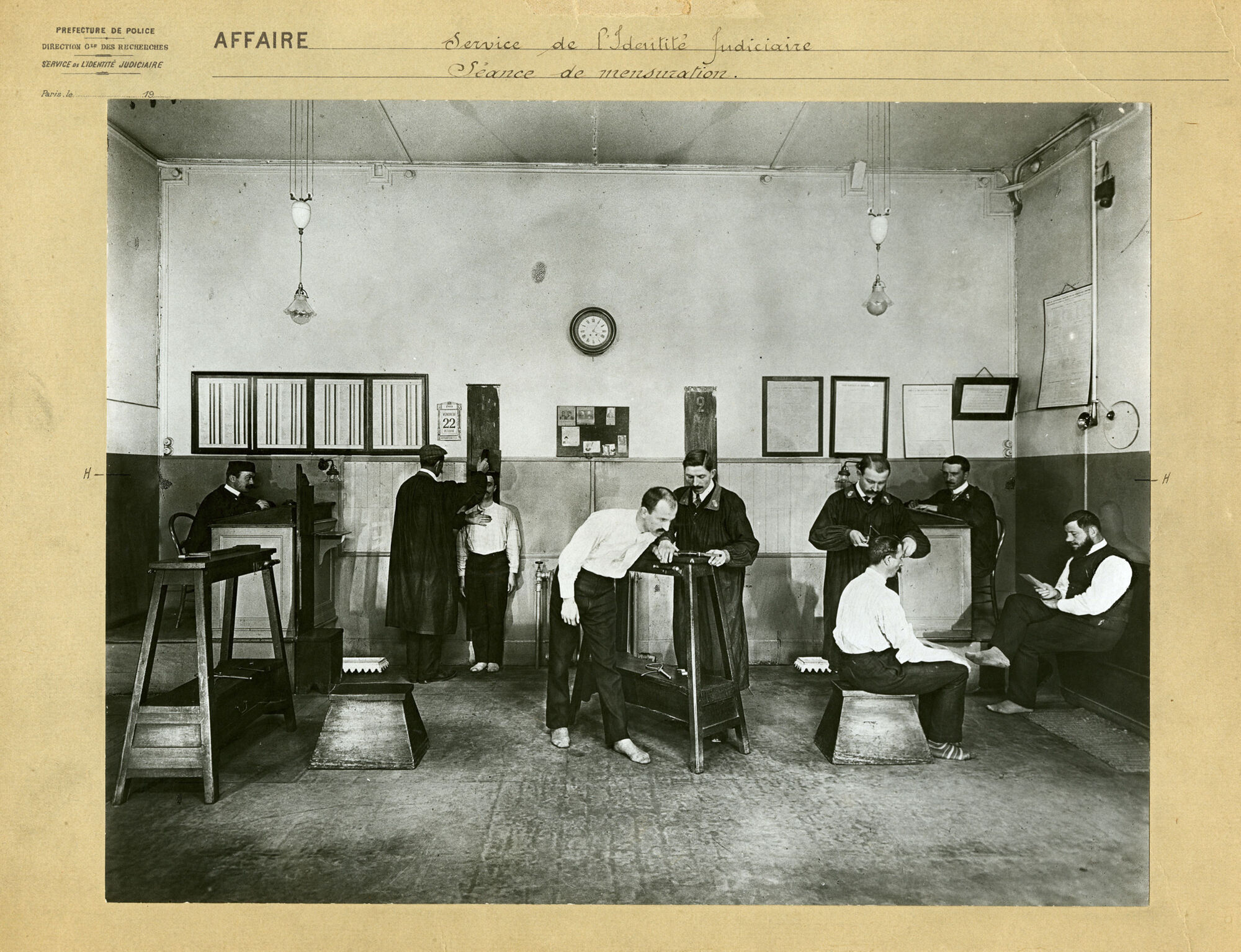 Vue photographique de la salle des mensurations du service parisien de l’Identité judiciaire dans laquelle des agents appliquent différentes formalités anthropométriques, fin XIXe - début XXe siècle.
Archives de la Préfecture de police de Paris, YB 5